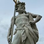 Beautiful marble statue of Neptune holding a trident, set against a cloudy sky, showcasing classical art.