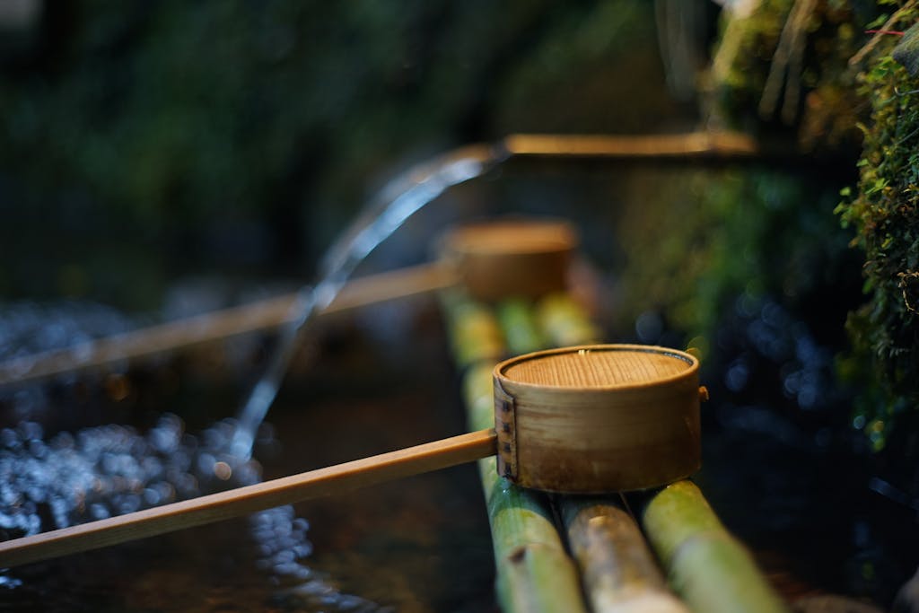 Photo by Ngeow Shen Sin Natural spring with clean water near bamboo pipes and wooden dippers in summer park