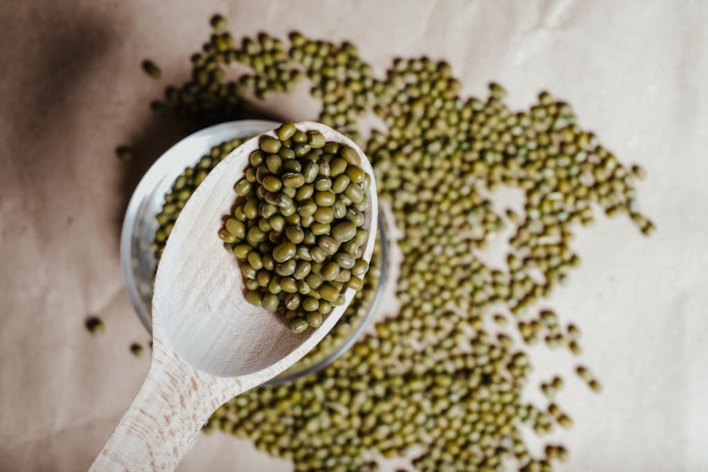 Photo by Vie Studio Top view of green mung beans on wooden spoon over scattered beans, emphasizing freshness and texture.